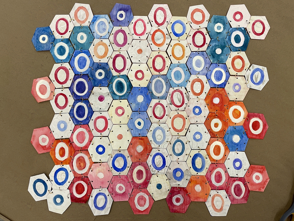 Multiple paper red, blue, and white hexagons with inscribed circles linked together. Front side.